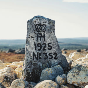 Kivipaasi, jossa tekstiä ja vuosiluku 1925, taustalla tunturimaisemaa.