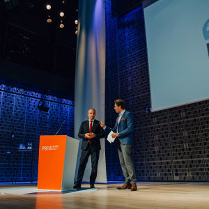 Two men talking to each other behind an orange podium on stage.