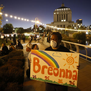 Demonstrant bär skylt med Breonnas namn. Person med ansiktsskydd bär skylt där det står Breonna.