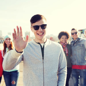 Fem stycken ungdomar står och vinkar mot kameran. Längst fram står en kille med solglasögon.
