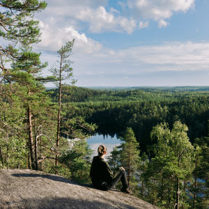 Nainen istuu kallioilla ja katsoo kohti järveä. 