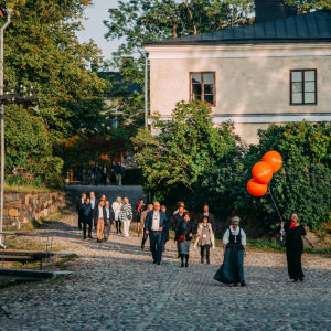 A person with three orange ballons leading a group of people in Suomenlinna.