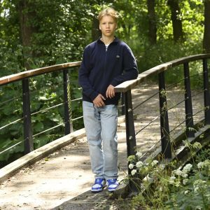 Tonårig pojke står på en bro i skogsdunge.