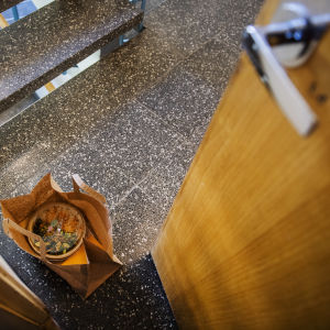 Bilden visar en papperspåse med hämtmat som lämnats framför dörren i ett trapphus. 