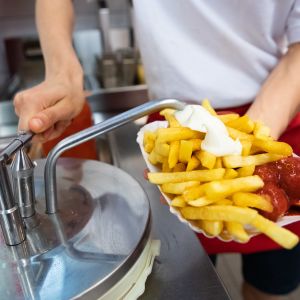 En anställd vid en snabbmatsrestaurang lägger majonnäs på pommes frites. 
