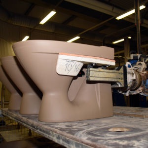 En blå robotarm placerar en wc-stol på ett bord i Ido badrums fabrik.