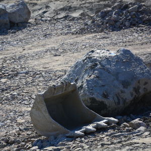 En grävskopa ligger på marken bredvid ett stort stenblock.