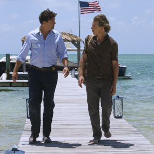 Bröderna John och Danny Rayburn spelas av Kyle Chandler och Ben Mendelsohn. Två män går på en brygga med turkost vatten och en amerikaflagga i bakgrunden.