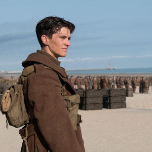 Tommy /Fionn Whitehead) står på stranden och i bakgrunden syns en massa andra soldater. 