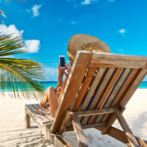 En kvinna i en solstol på en strand sitter och petar på en smarttelefon.