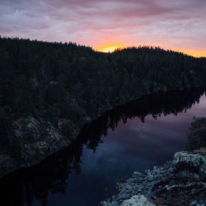 Auringonlasku Suomessa, kalliomaisema, havumetsä ja järvi.