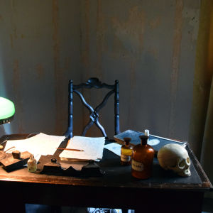 Installation som föreställer prof. Saelans skrivbord Gammalt skrivbord med lampa, apoteksflaskor, anteckningar, bläckpenna.