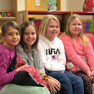 Matilda Sandgren, Isa Sundell, Lydia Norrgrann och Aura Lindgren sitter på en röd soffa. 