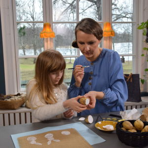 Pensla textilfärg på stämplar skurna av potatis och tryck mönster med dem. Kvinna och barn trycker tygtryck med potatis