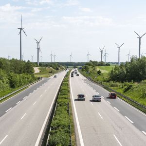 Bilar som kör på tyska motorvägen Autobahn A20 med vindkraftverk i bakgrunden. 