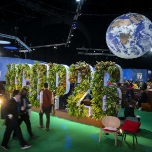 Människor rör sig på klimatmötet i Glasgow - en skylt med växter syns och en jordglob i hörnet av bilden.