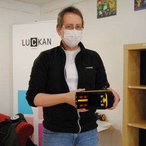 Man med kort ljusbrunt hår och svart tröja står visar upp en kamera byggd av legobitar.