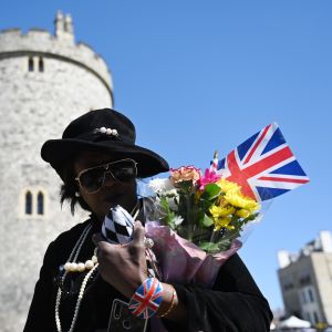 En person med solglasögon bär på en brittisk flagga och gula och rosa blommor.