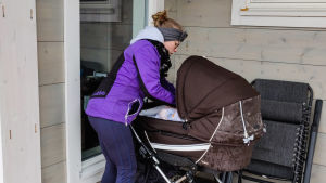 Efter att ha fått komma ner i vagnen och blivit skuffad omkring en stund sover Bönan lugnt igen. Själv har hon inget hum om det inhiberade dopet. En kvinna i lila jacka sköter om en baby som ligger i en barnvagn.