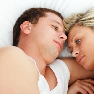 Man och kvinna ligger vända mot varandra i en säng, ser fundersamma ut