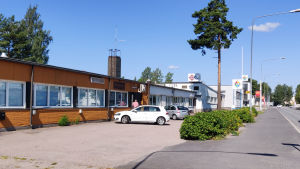 Alla hus som syns på bilden hör till samma fastighet. Längst bort syns färgaffären. Vy av affärslokaler invid en gata: Ett lågt hus i gult och vitt, sedan ett större vitt hus.