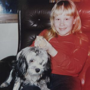 Elisa Aaltola lapsena, lemmikkikoiran kanssa kotona nahkatuolissa.