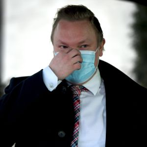 Kulturminister Antti Kurvinen med munskydd på sig. Han står framför Ständerhusets dörr och pratar med reportrar.