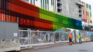 Färggrant i höstrusket. Bild på det nya, ännu halvfärdiga barnsjukhusets fasad. Framför det stängsel och två buggarbetare.