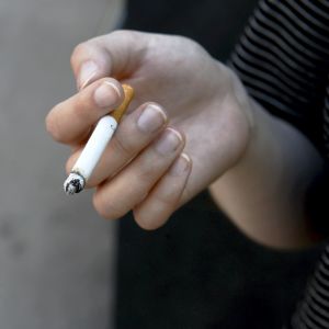 Hand som håller i en rykande cigarett.