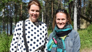 Rita Danielsson (till vänster) och Susann Airisvaara jobbar båda som finsklärare i Ekenäs gymnasium. Rita har närmare 20 års erfarenhet bakom sig, medan Susann har jobbat i Ekenäs gymnasium sedan 2005, det vill säga från det att det andra inhemska språket blev frivilligt i studentexamen. Två kvinnor står bredvid varandra ich tittar leende mot kameran. Utomhus, sommar. Skog och strand och vatten i bakgrunden.