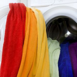 Handdukar i regnbågsflaggans färger hänger ut från en tvättmaskin.