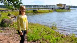 Helmi Parviainen tycker att det är roligt att sova i tält och att vara på bilsemester. En flicka som står på stranden framför vattnet och en lång brygga.