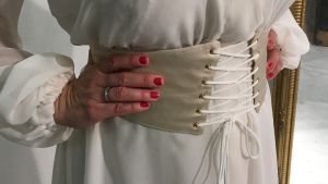 En detalj från Janina Frys klänning. Ett korsettbälte av siden pryder den vita, transparenta klänningen. En vit klänning med korsettbälte.