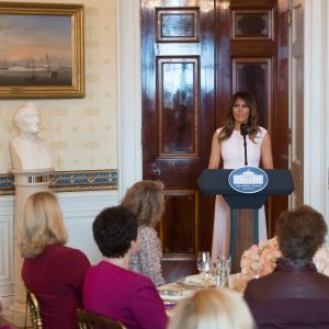 Melania Trump talar till guvernörernas hustrur. Melania Trump i en talarstol i Vita huset. Guvernörernas hustrur sitter vid dukade bord i ståtlig omgivning.