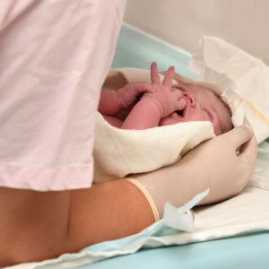 A newborn baby cradled on a table by a health care worker.