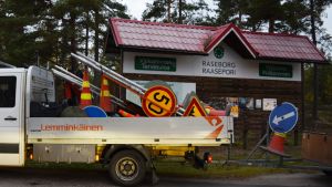 Välkommen till Raseborg! Men ta tid på dig för här utförs en mängd vägarbeten just nu. Vägmärken på ett flak framför skylten som välkomnar besökaren till Raseborg.