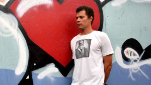 Ungdomsledare Sebastian Berg visar i en av utmaningarna på Instagram hur du kan sätta på dig en t-shirt medan du står på händerna. Man i vit t-skjort framför gatukonstverk.