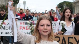 Belarusier av olika generationer och yrkesgrupper står enade En blond kvinna håller upp en bukett med vita blommor i ett demonstrationståg i Belarus.