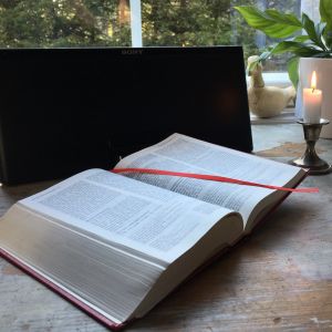 Uppslagen bibel och ett tänt ljus vid en radio.