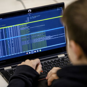 En person fotograferad bakifrån medan han sitter vid en dator och kodar.