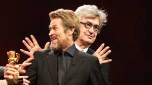Willem Dafoe och den gyllene björnen - och Wim Wenders, som sprider ut ett par vingar bakom Dafoes rygg. Willem Dafoe får sin hedersbjörn under filmfestivalen Berlinale 2018.