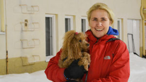Hundterapeut Christina von Pfaler med pudeln Nilla. En kvinna i röd jacka står utomhus och håller i en brun pudel.