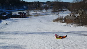 Ada Viljanen surfar nerför backen utan rädsla. Barn som glider ner för borgbacken i borgå med pulka