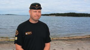 Rasmus Friman, vicestationschef vid Nagu sjöbevakningsstation, säger att drönaren hjälper gränsbevakningen att spara tid i arbetet., En man i sjöbevakningens mörka arbetskläder står på stranden vid havet.