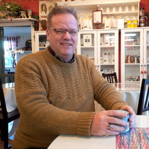 Gustav Söderström driver ett ekologiskt värdshus och kafé i Sibbo. Man sitter vid ett bord med kaffekopp i ett kafé.