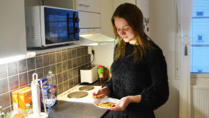 Några pepparkakor finns kvar från pepparkaksbaket som Aino Kiuru organiserade. Det blev så många pepparkakor att de kunde delas ut bland de boende som inte själva varit med och bakat. En kvinna står i ett kök och håller i ett fat met pepparkakor. Hon har blicken riktad ner mot fatet.