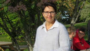 Jennie Ahtola tycker att ovissheten är jobbig, men berömmer sin personal för att alla orkar hålla humöret uppe. En kvinna med brunt hår och glasögon på en gård, där det finns skolelever i bakgrunden, men man ser dem inte så bra.
