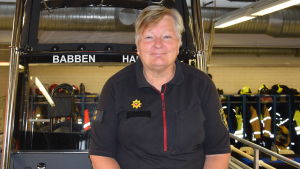 Babben sitter i Babben. Barbro Eskelin är trotjänare vid räddningsverket. en kvinna sitter i fören av en räddningsbåt. Båten befinner sig på torra land, inne i en hall, Hangö brandstation.