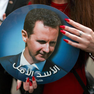 En kvinna som håller i ett porträtt av Syriens president Bashir al-Assad.  
