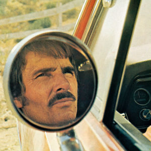 Autoa ajava viiksekäs mies (näyttelijä Dennis Weaver) katsoo tiukasti sivupeiliin, jonka kautta hänet on kuvattu. Kuva elokuvasta Kauhun kilometrit.